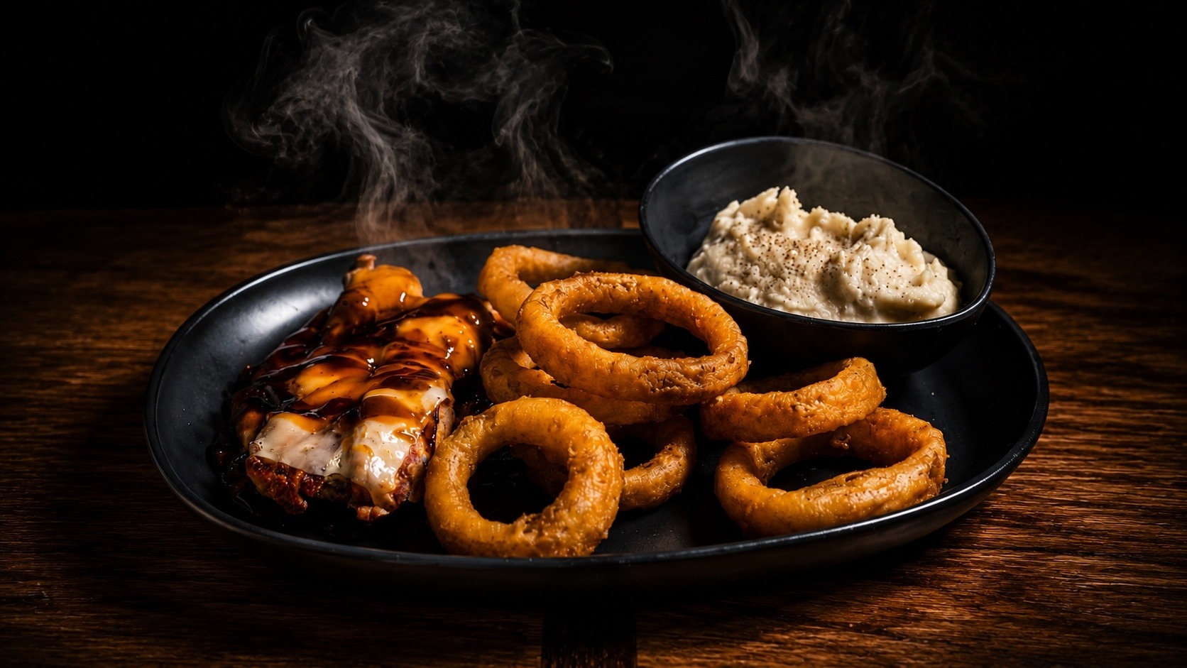 BBQ chicken with onion rings and mashed potatoes, steam rising from a black plate