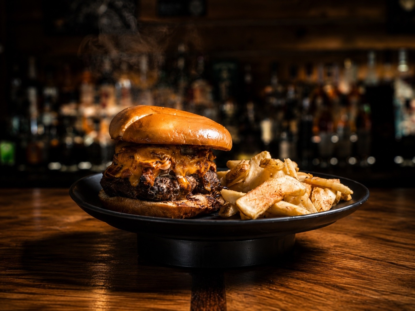 Pulled pork cheeseburger with steak fries on a black plate